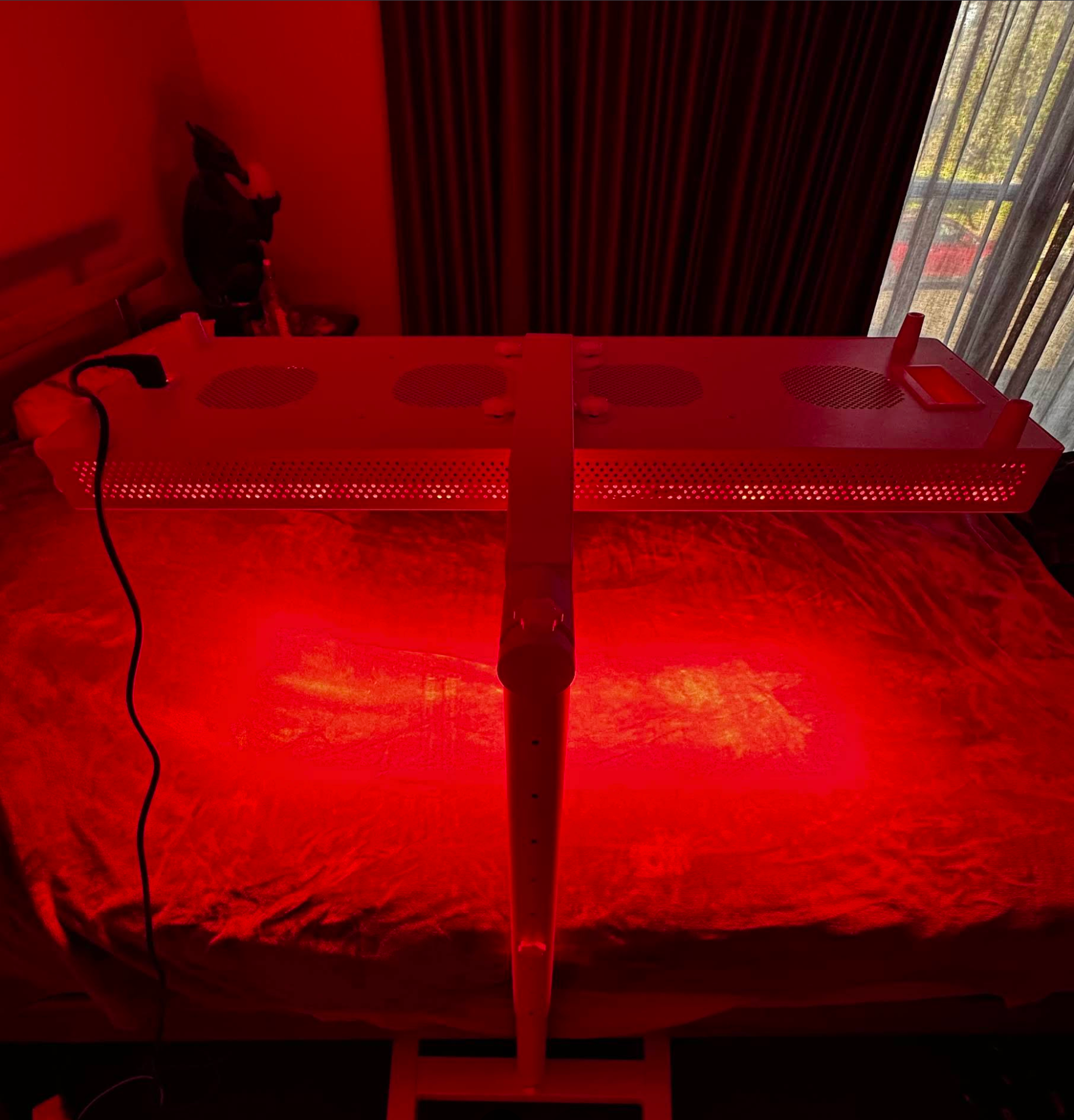 Hero300 red light therapy panel by Red Light Hero on a HS4 Branch Stand over a bed in a dimly lit room