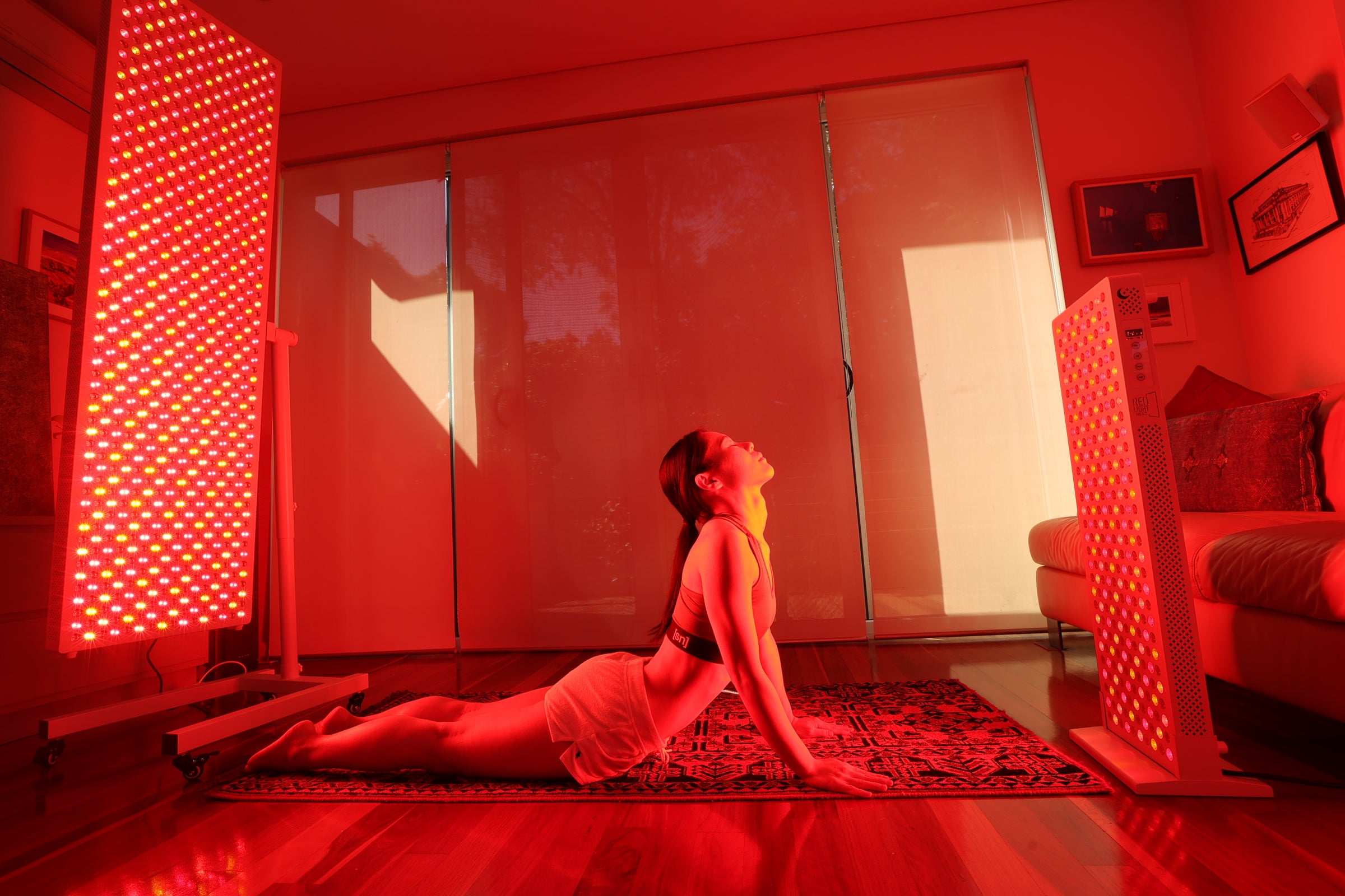 Person in a red-lit room performing a yoga pose on a rug in front of Hero960 Elite and Hero300 Elite panels on a HS4 Branch Stand and HS1 Floor Stand respectively..