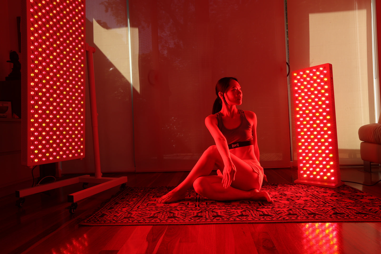 Person sitting on a mat in a room with red light therapy panels.