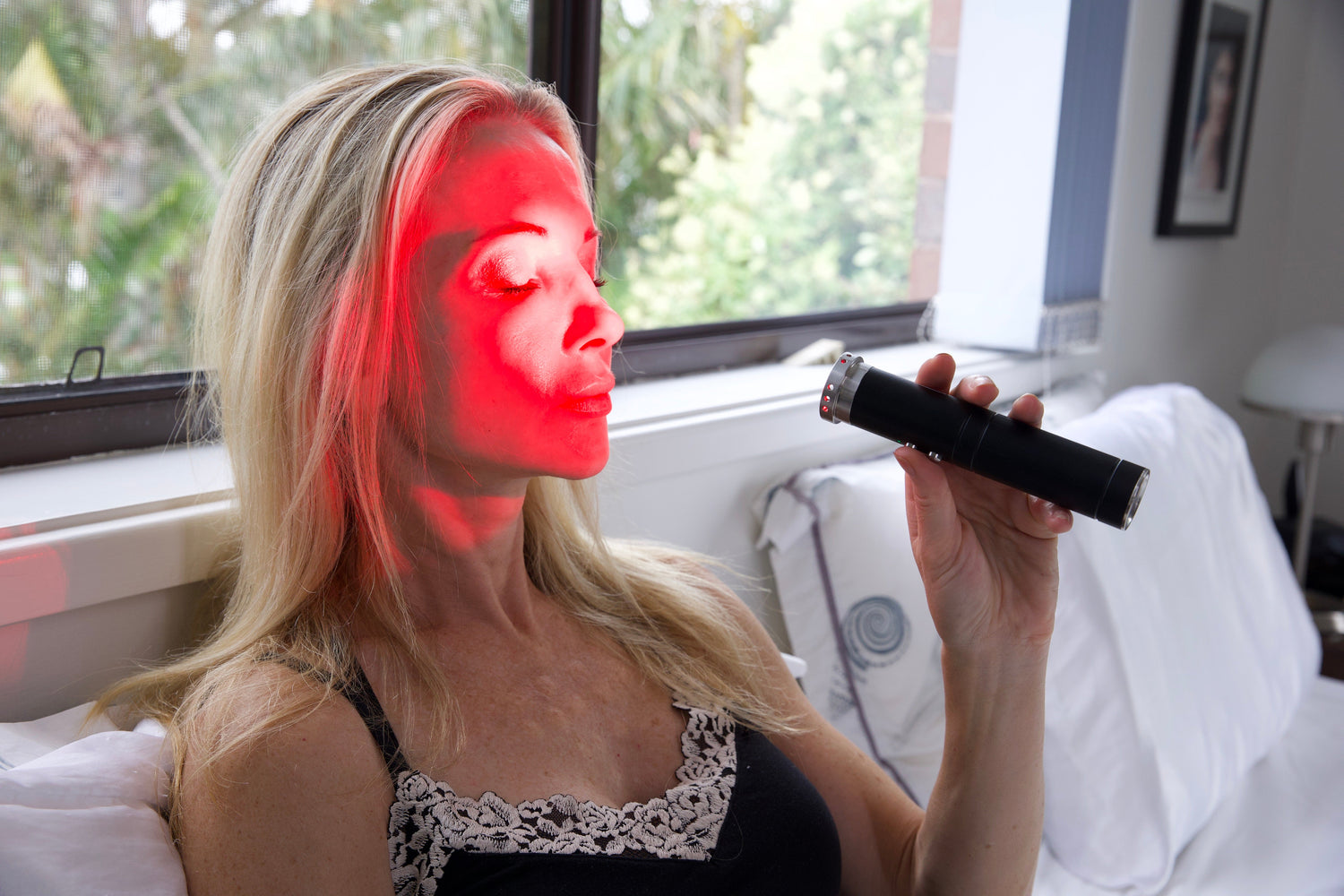 Woman using a HeroTorch red light therapy device on her face