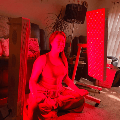 Woman sitting in her lounge room between 2 Hero300 red light therapy panels by Red Light Hero - a red light therapy brand trusted and loved by many customers - one on a HS1 Floor Stand the other on a HS4 Branch Stand