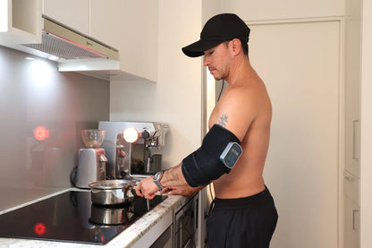 Man wearing a red light therapy arm wrap while cooking
