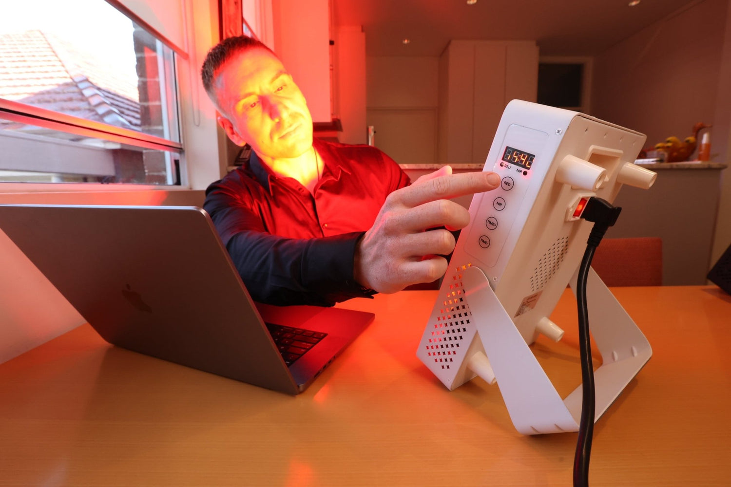 Man working at a laptop with a white Hero60 Elite panel beside him casting red light on his face