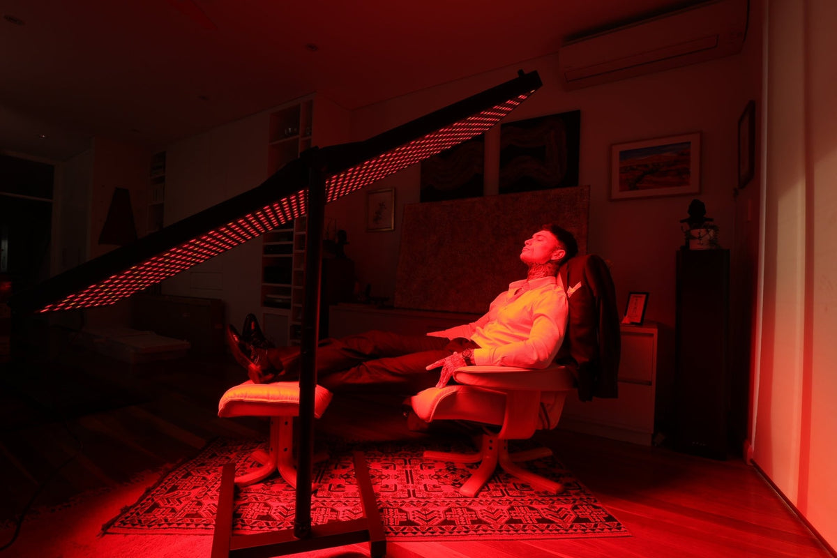 Person seated under a horizontal red light therapy panel on the HS4 stand
