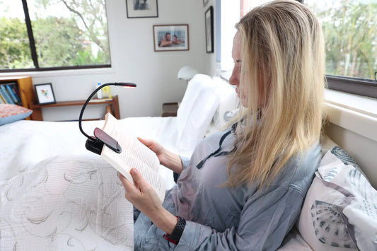 Woman reading in bed with a HeroReader lamp clipped to her book