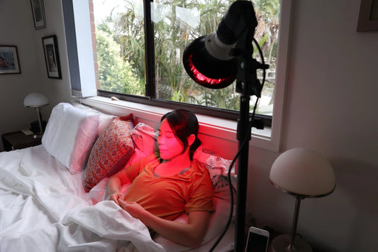 Woman relaxing in bed under a HeroSpotlight red light therapy lamp