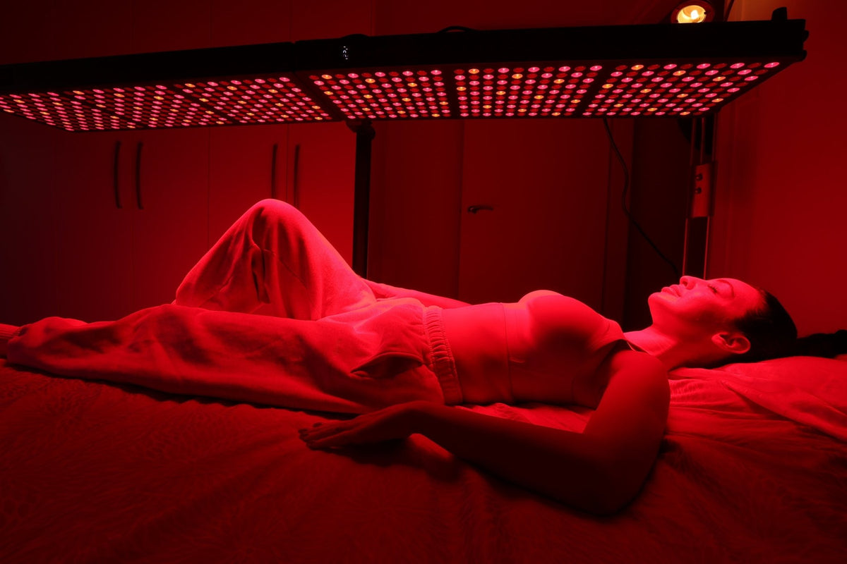 Person lying beneath a horizontal red light therapy panel
