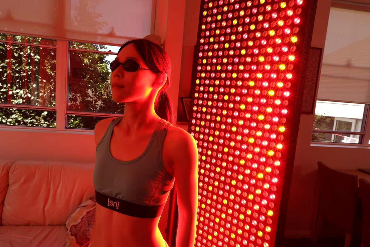 Woman standing beside a red light panel while wearing protective glasses