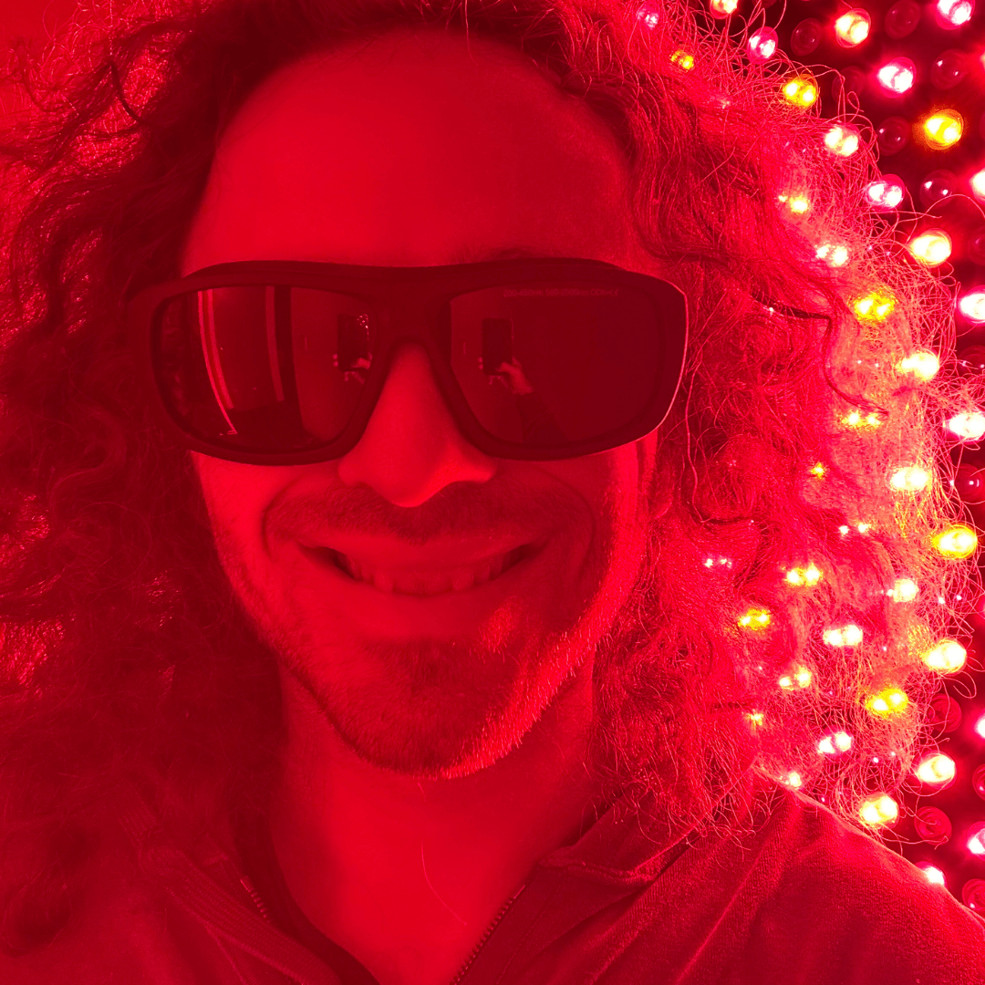 Man smiling in protective glasses beside an illuminated red light panel