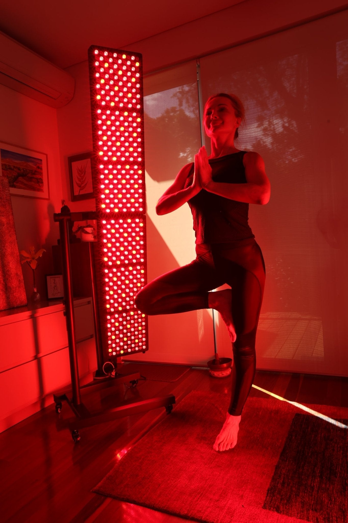 Woman in tree pose beside an illuminated Hero300 panel