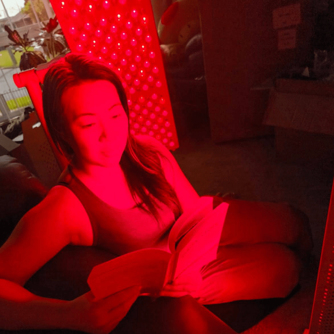 Woman relaxing in red light beside an illuminated Hero300 panel